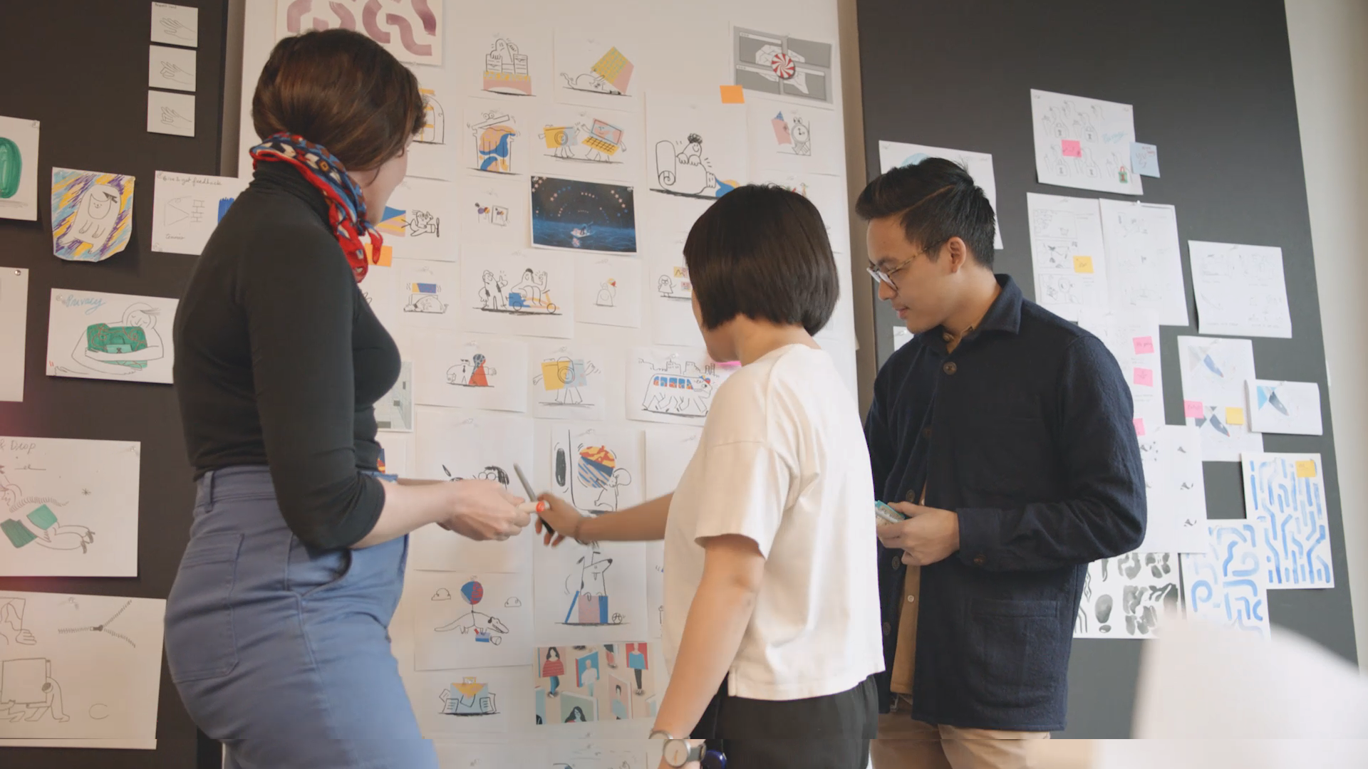 three members of the Dropbox team look at a wall with illustrations posted to it